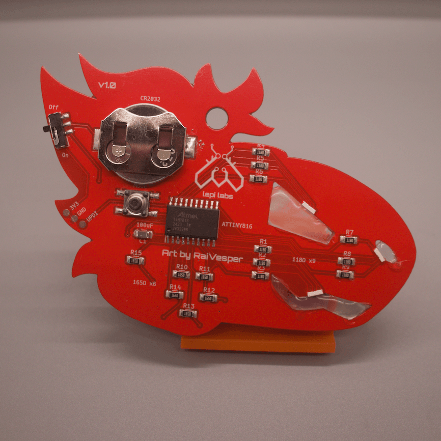 Photo of the rear side of a red PCB badge in the shape of a protogen's head. Many components are shown, including RGB LEDs with hot glue diffusers for the facial features, a coin cell battery, microcontroller, LEDs and resistors, push button and sliding switches, and a UPDI connector.